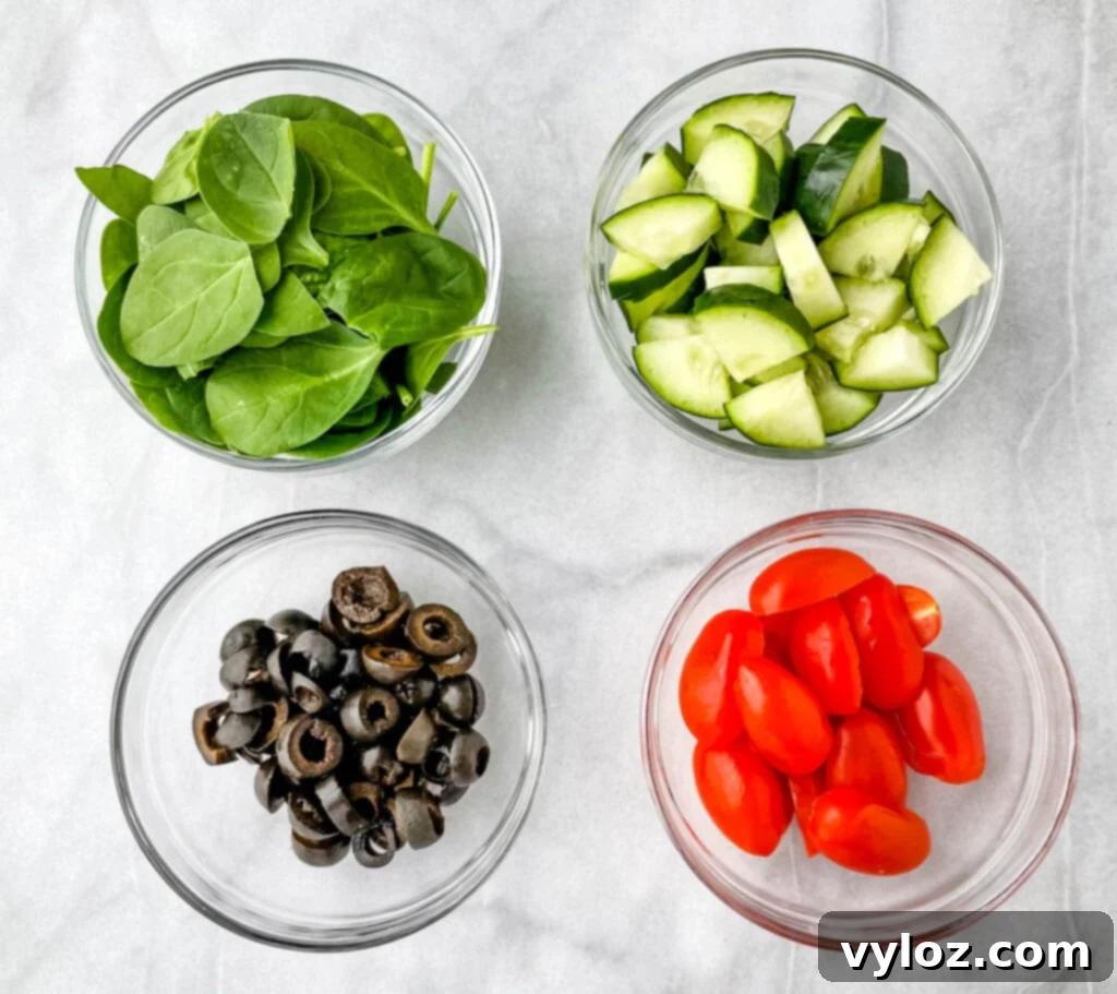 fresh spinach, chopped cucumbers, black olives, and tomatoes in separate glass bowls