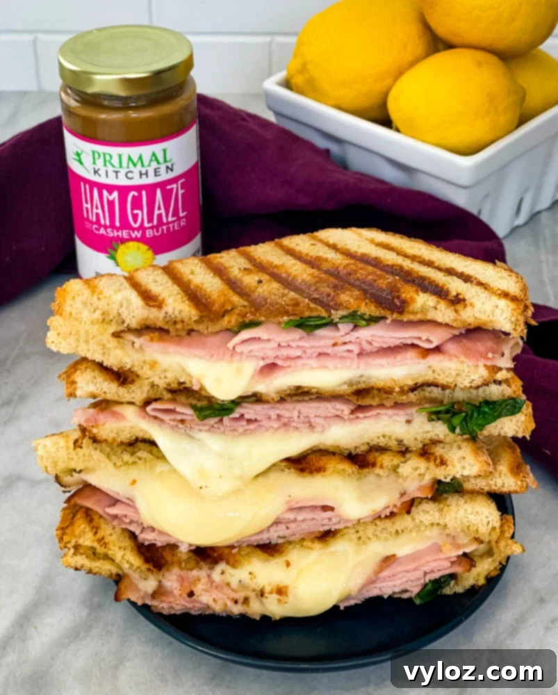 Perfectly sliced ham and cheese panini sandwich on a rustic plate, revealing its layers of ham, melted cheese, and crisp sourdough bread.