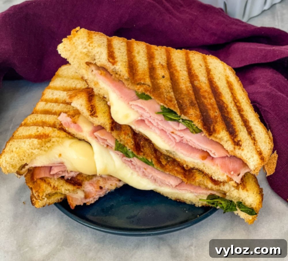 The final delectable ham and cheese panini, sliced and presented on a plate for immediate enjoyment.