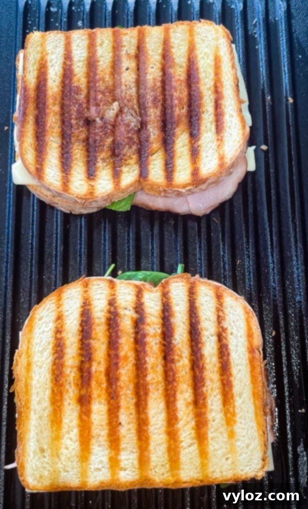 An assembled ham and cheese panini sandwich on a grill pan, layered with ham, cheese, and spinach, ready for cooking.