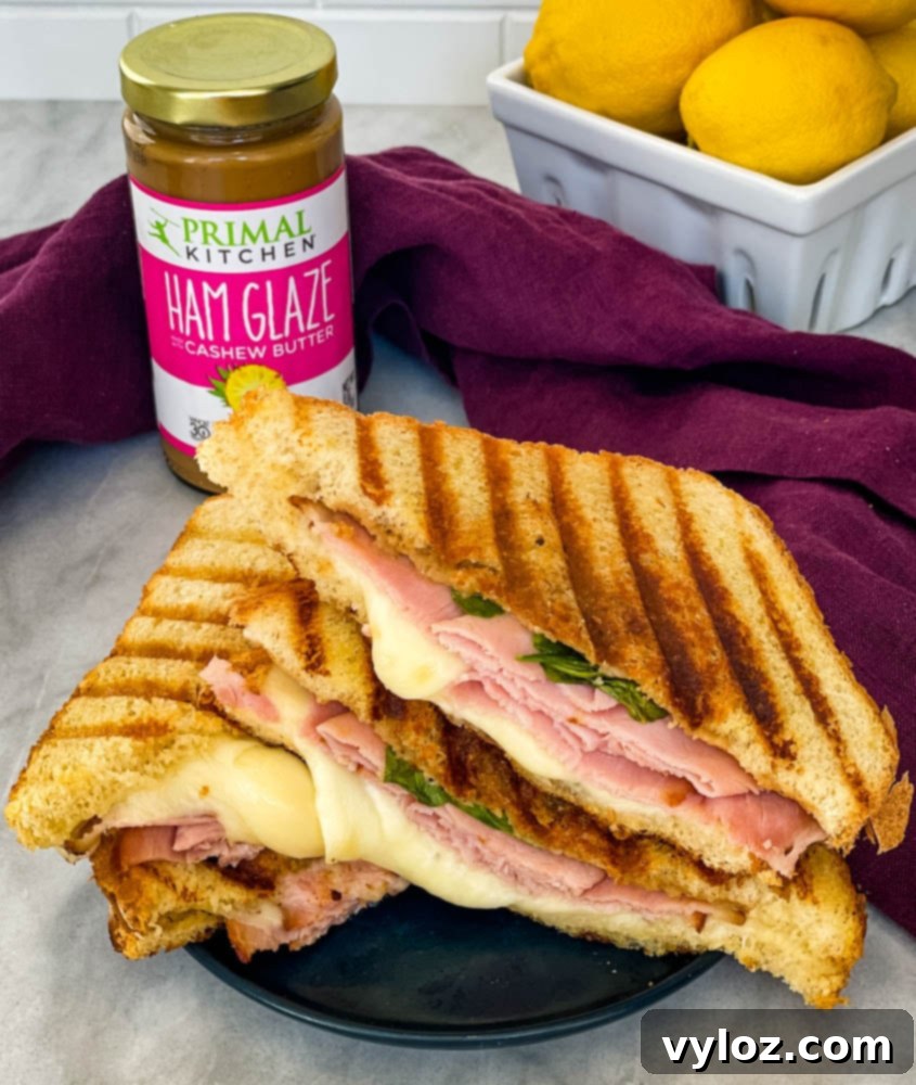 A beautifully presented, sliced ham and cheese panini, showcasing its perfectly melted cheese, savory ham, and fresh spinach layers.