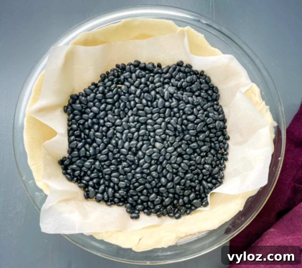 A pie crust covered with parchment paper and filled with pie weights, undergoing the blind baking process.