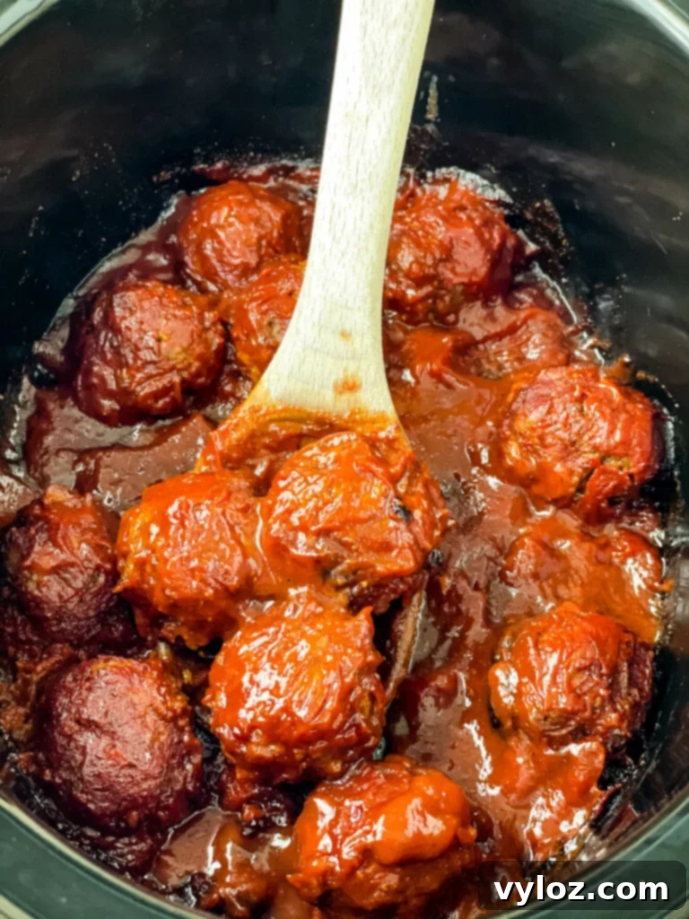 Set-It-and-Forget-It BBQ Meatballs 2 BBQ meatballs simmering in a slow cooker, ready to be served with a wooden spoon