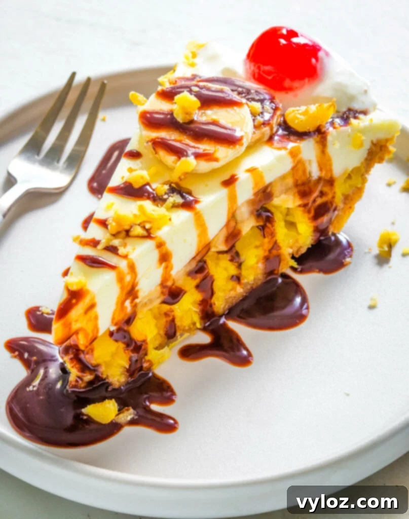A beautifully presented slice of banana split pie, richly topped with whipped cream, a cherry, and a generous drizzle of chocolate syrup, showcasing its tempting layers.