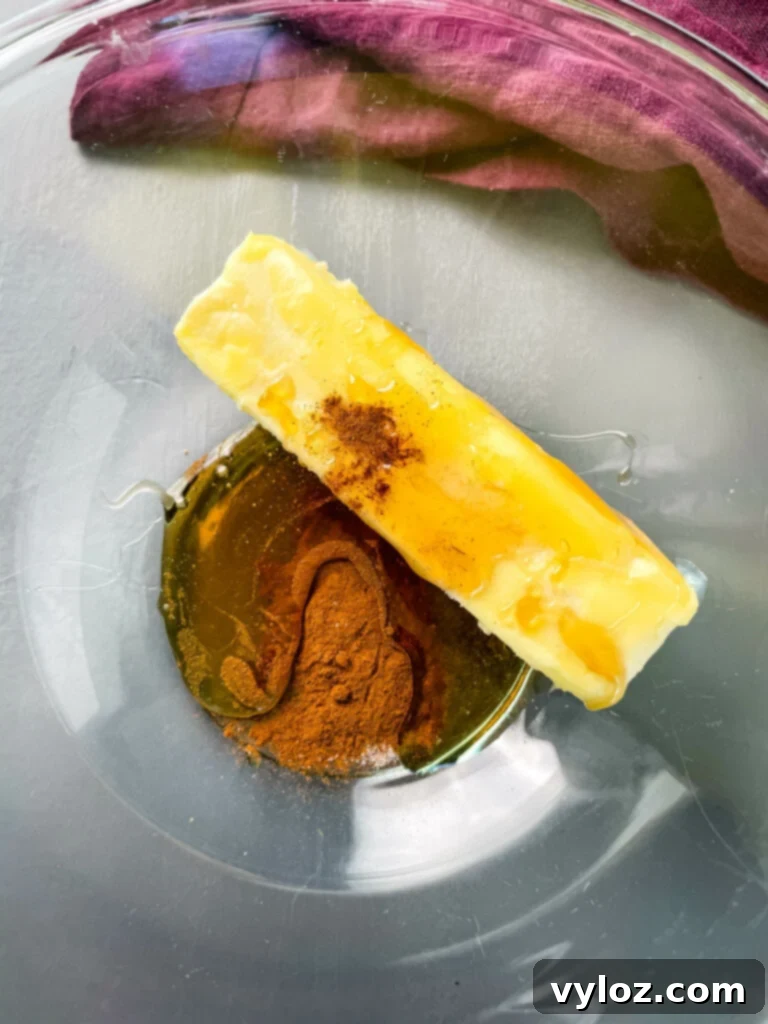 Butter, cinnamon powder, and golden maple syrup are combined in a glass mixing bowl, ready to be whipped into maple butter.