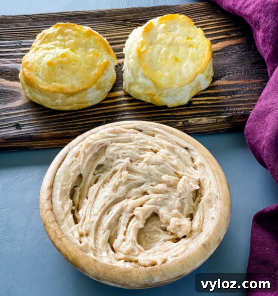 Close-up of golden-brown biscuits spread with creamy maple butter and drizzled with extra maple syrup, enticing for a sweet breakfast.