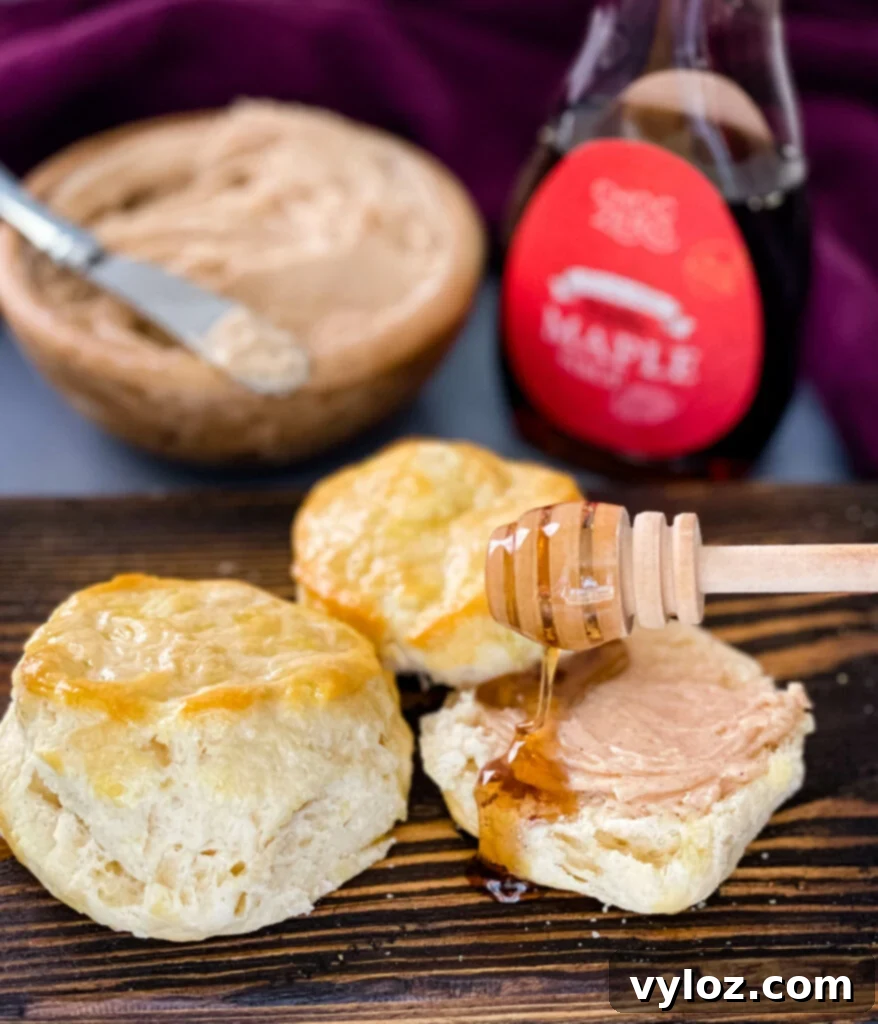 Close-up of golden-brown biscuits spread with creamy maple butter and drizzled with extra maple syrup, enticing for a sweet breakfast.