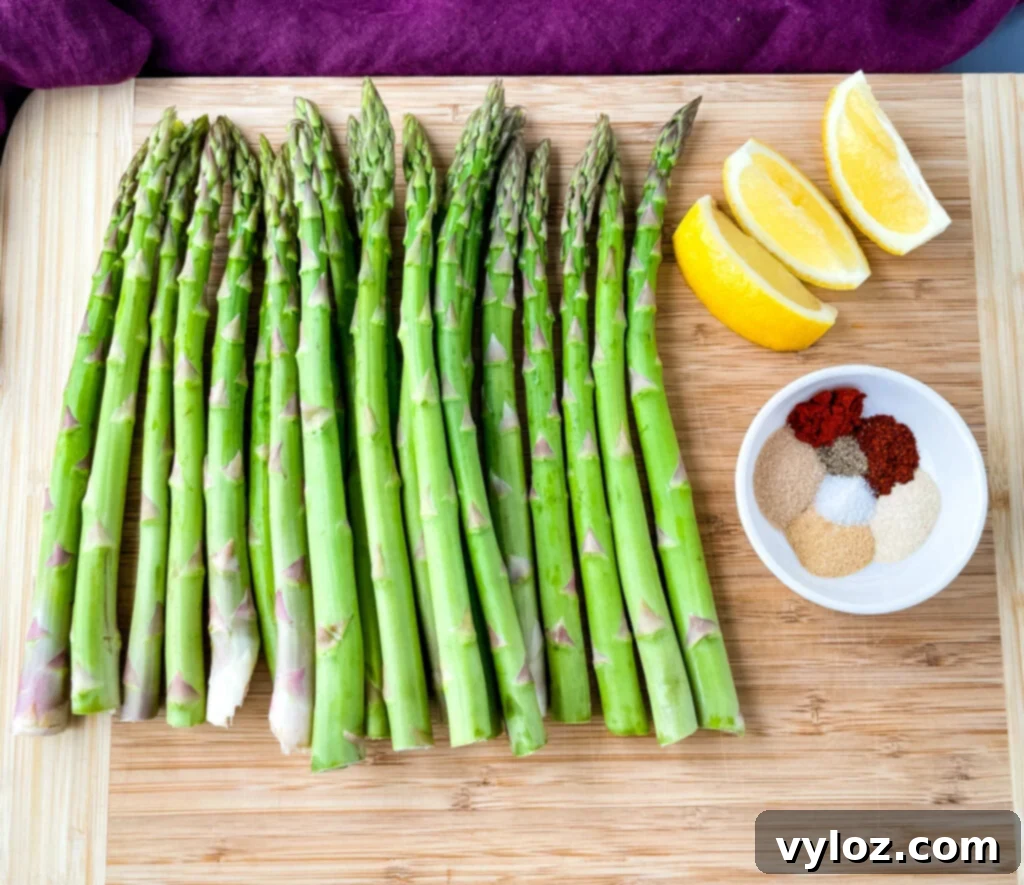 Grilled Asparagus Foil Packets 3 Raw asparagus spears on a wooden cutting board with lemons and a bowl of homemade BBQ seasoning