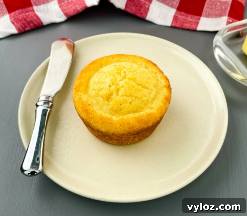 A single cornbread muffin presented neatly on a white plate, ready to be eaten.