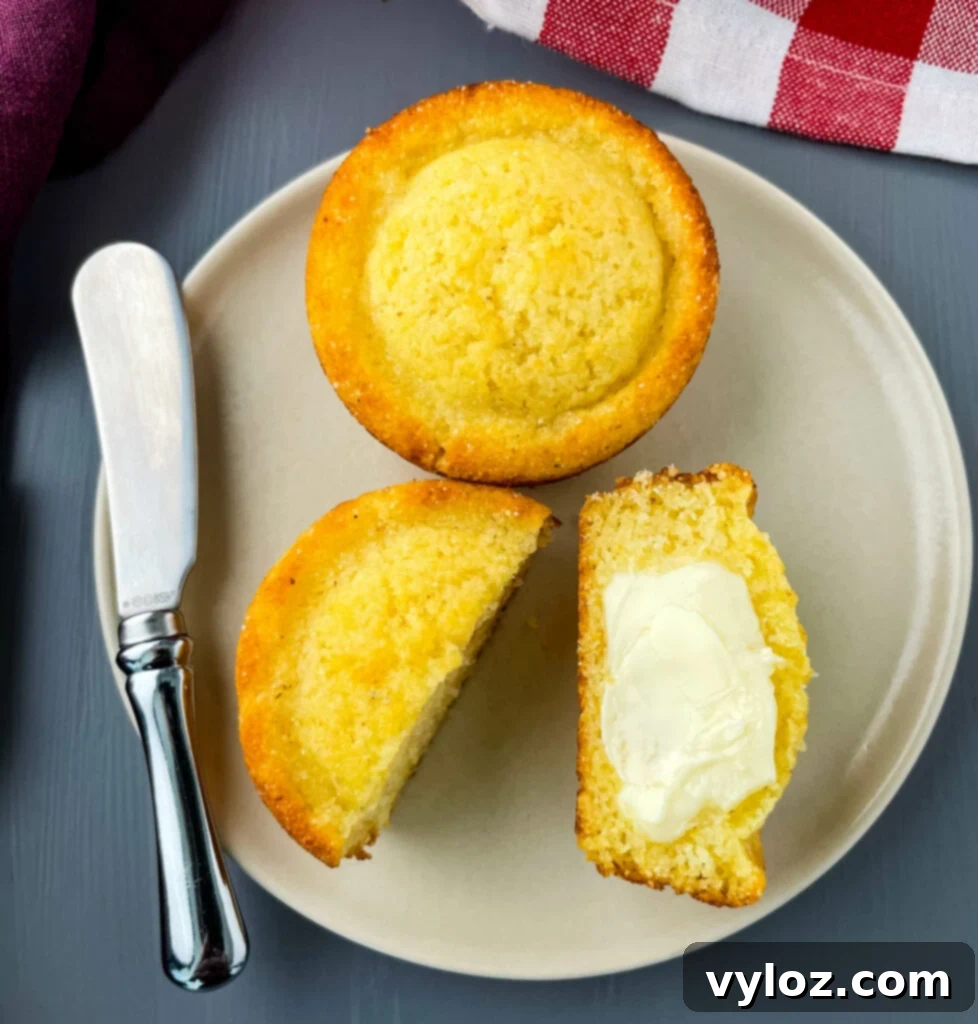 A cornbread muffin sliced in half and drizzled with warm butter, showcasing its moist texture.