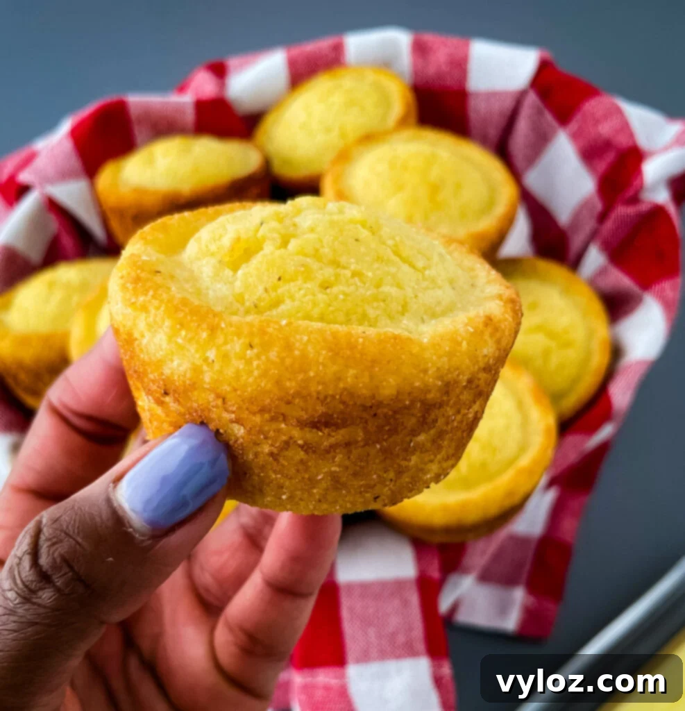 A person holding a freshly baked cornbread muffin, showcasing its golden crust.