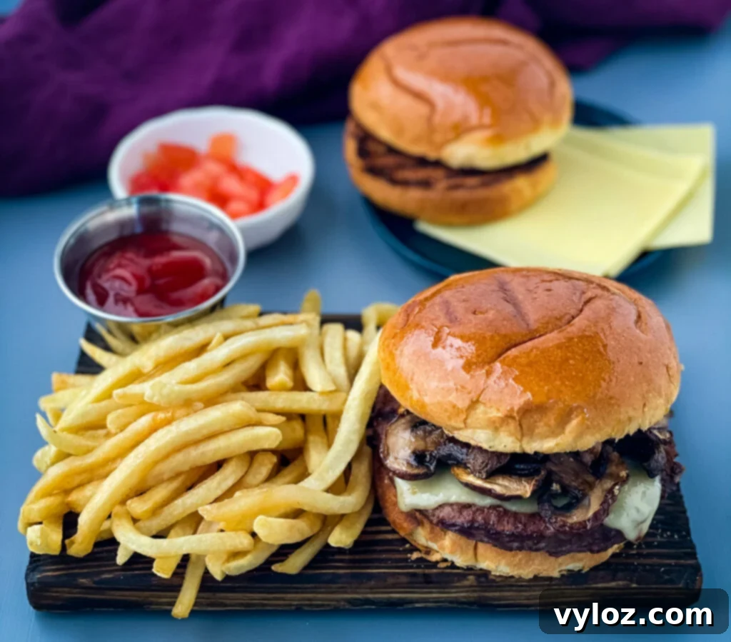 Savory Mushroom Swiss Burger 2 A delicious Mushroom Swiss Burger served on a plate with crispy French fries, highlighting the melted Swiss cheese and sautéed mushrooms.