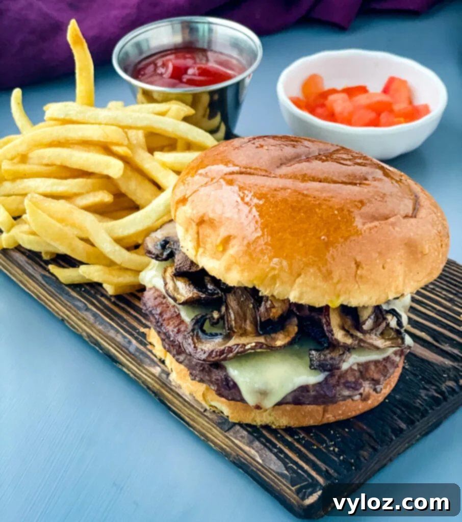 Savory Mushroom Swiss Burger 9 A perfectly cooked Mushroom Swiss Burger on a plate with crispy French fries, ready to be enjoyed.