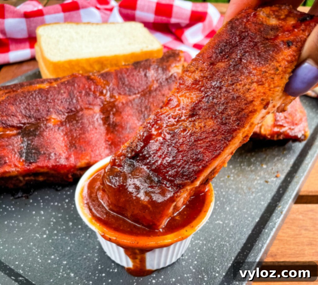 Person holding a perfectly grilled baby back rib with BBQ sauce