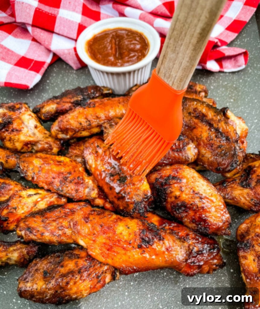 Perfect Grilled Chicken Wings 12 Grilled chicken wings being glazed with BBQ sauce using a cooking brush