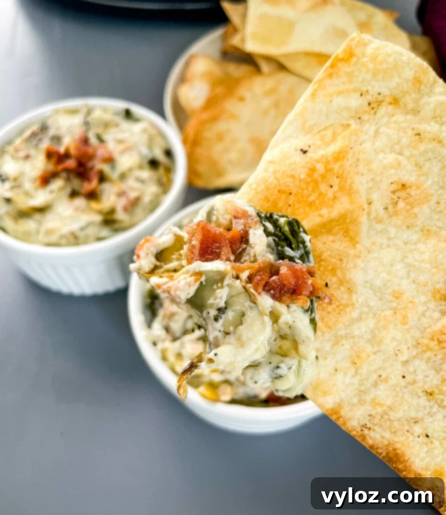 person holding bacon spinach artichoke dip on a chip