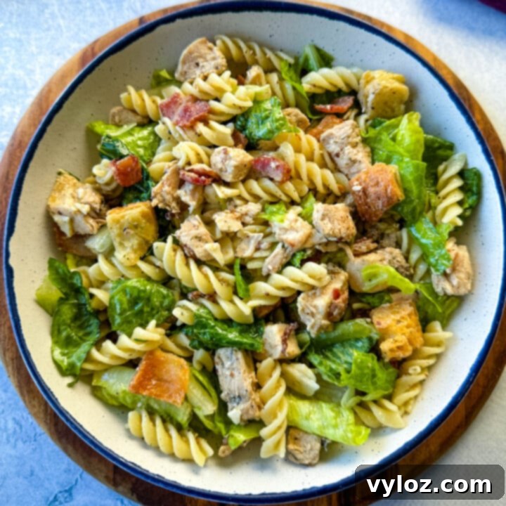 A large, inviting bowl of Chicken Caesar Pasta Salad, prominently featuring perfectly cooked pasta, tender chicken, crisp Romaine lettuce, and grated Parmesan.