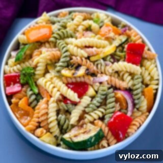 Grilled vegetable pasta salad in a white bowl, garnished with fresh herbs