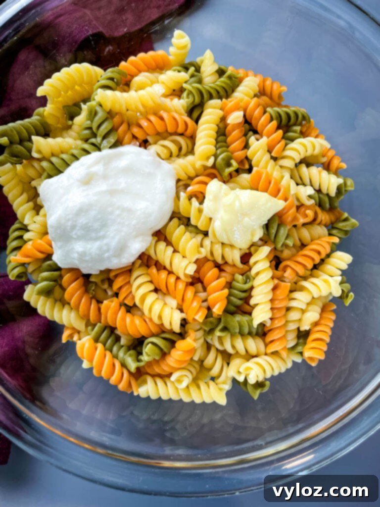 Close-up of dry rotini pasta, showcasing its tri-color and twisted shape, held in a glass bowl