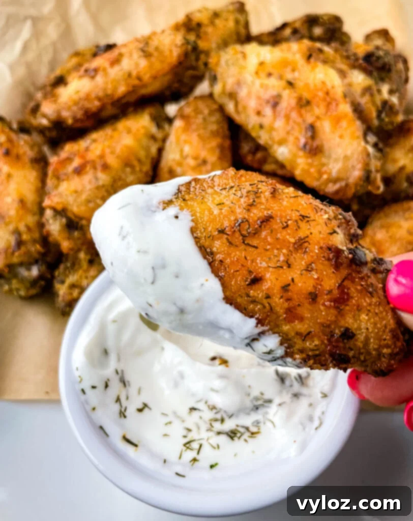 A person presenting a plate of crispy ranch chicken wings with a bowl of ranch dressing, emphasizing their delicious appeal.