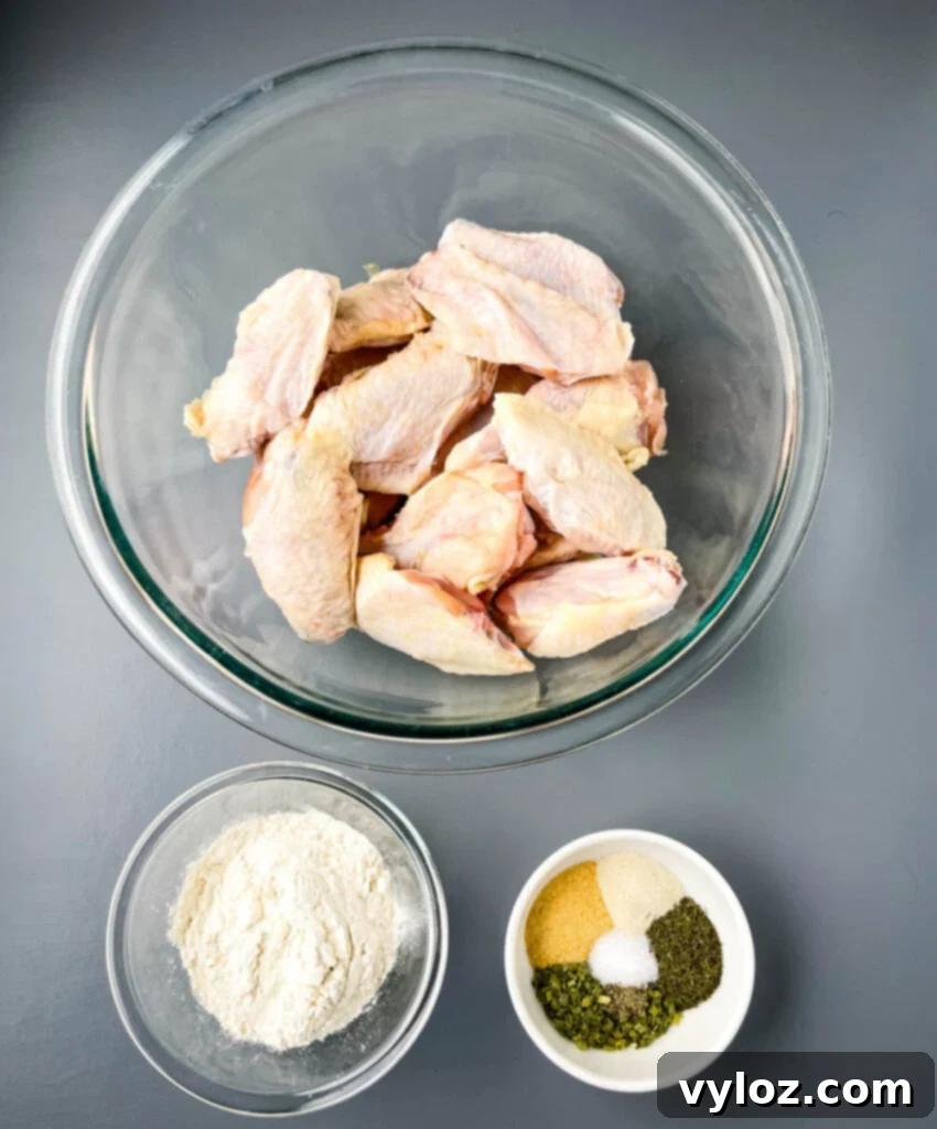 Bowls containing raw chicken wings ready for seasoning, next to a bowl of freshly prepared homemade ranch seasoning mix.