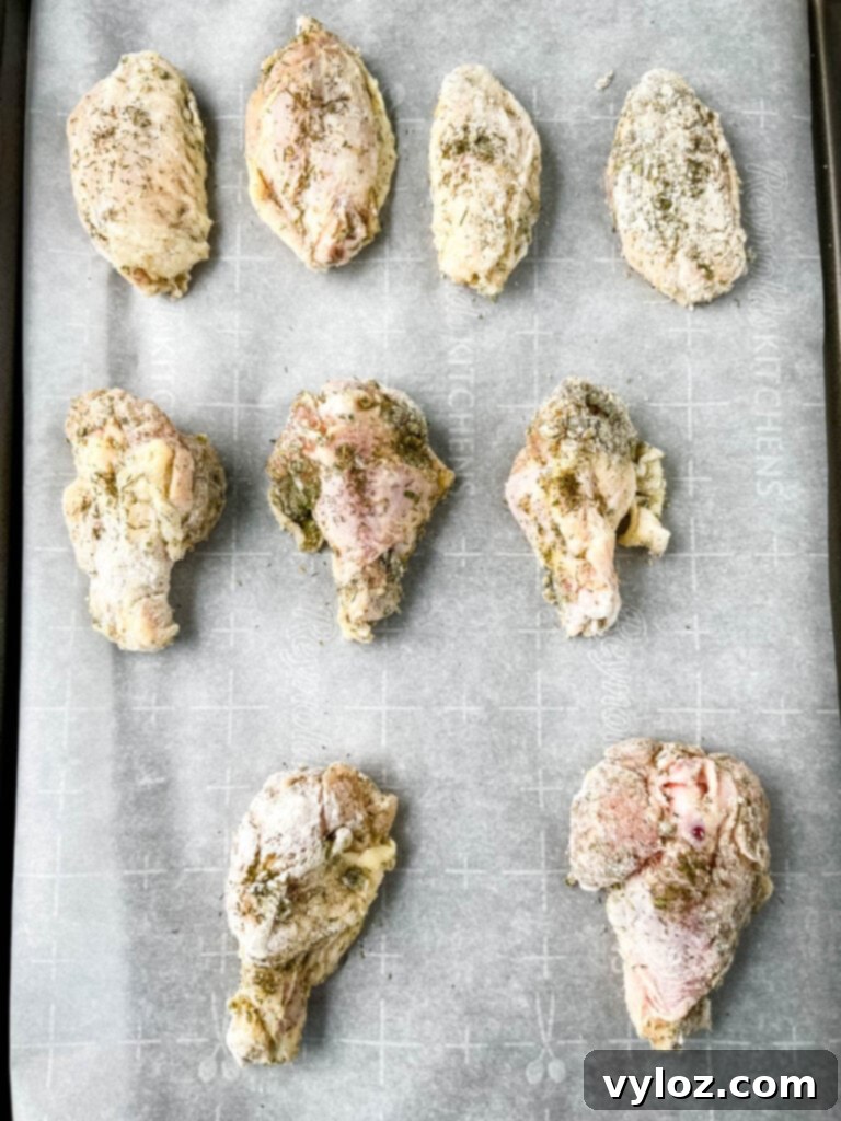 Raw ranch seasoned chicken wings neatly arranged on a parchment-lined baking sheet, prepared for oven baking.
