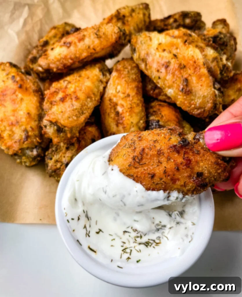 A hand holding a crispy ranch chicken wing, perfectly dipped into a bowl of creamy ranch dressing.