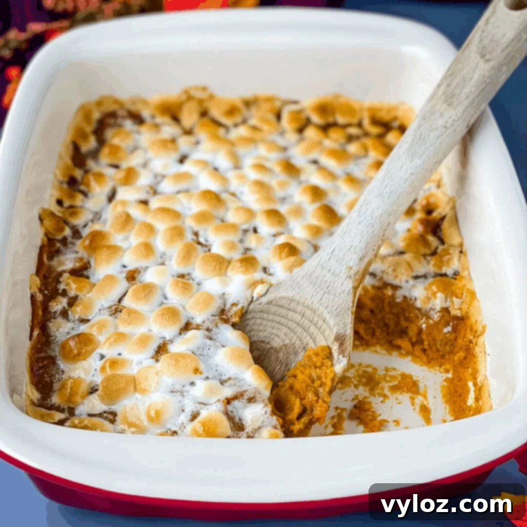 spoonful of sweet potato casserole with marshmallows in a red baking dish