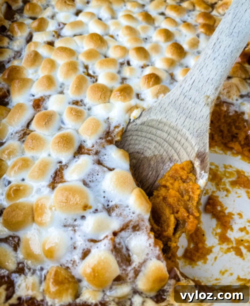 spoonful of sweet potato casserole with marshmallows in a red baking dish