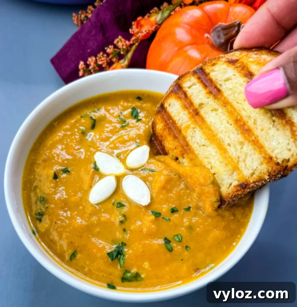 Quick Creamy Pumpkin Soup with Canned Pumpkin 6 person dipping a slice of crusty bread into a steaming bowl of canned pumpkin soup