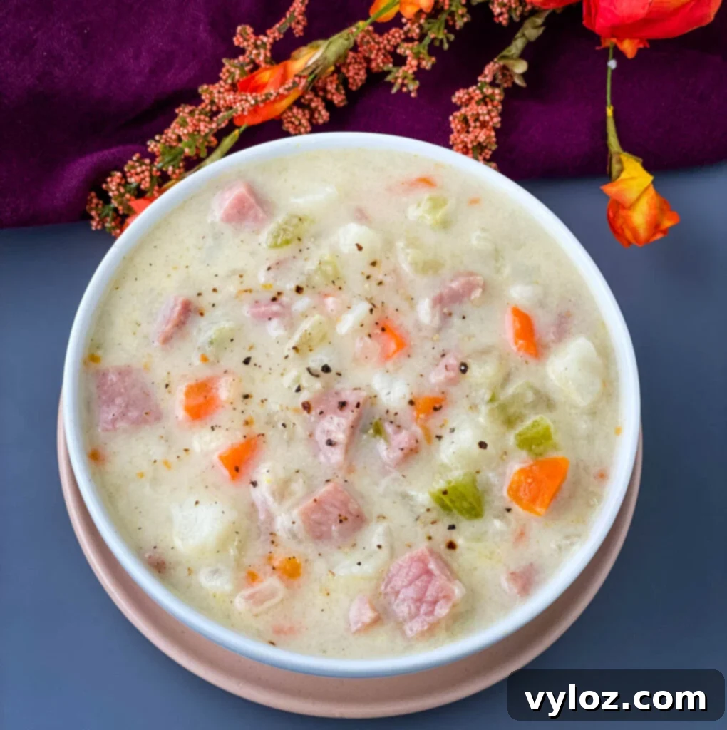A rustic white bowl filled with creamy ham, potato, and vegetable soup, garnished with fresh herbs, offering a visually appealing and comforting meal.