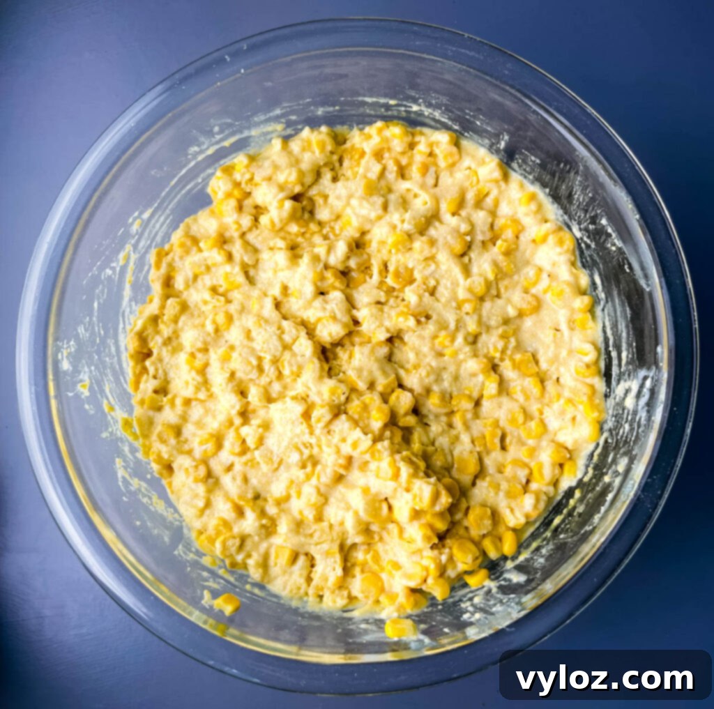 A generously filled glass bowl of unbaked corn casserole batter, showcasing its rich texture and ready to be transferred to a baking dish.