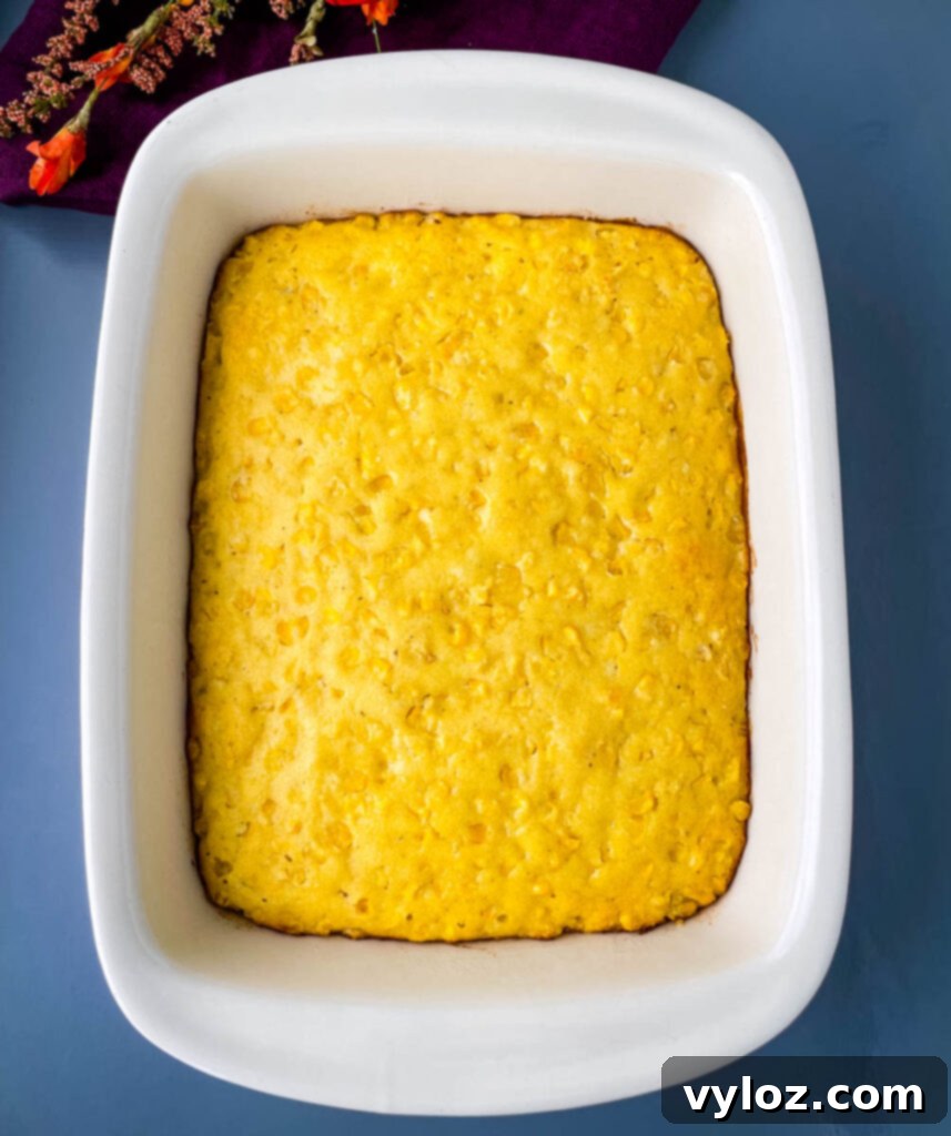 A fully baked, golden-brown corn casserole, fresh out of the oven and resting in a ceramic baking dish, ready to be sliced and served.
