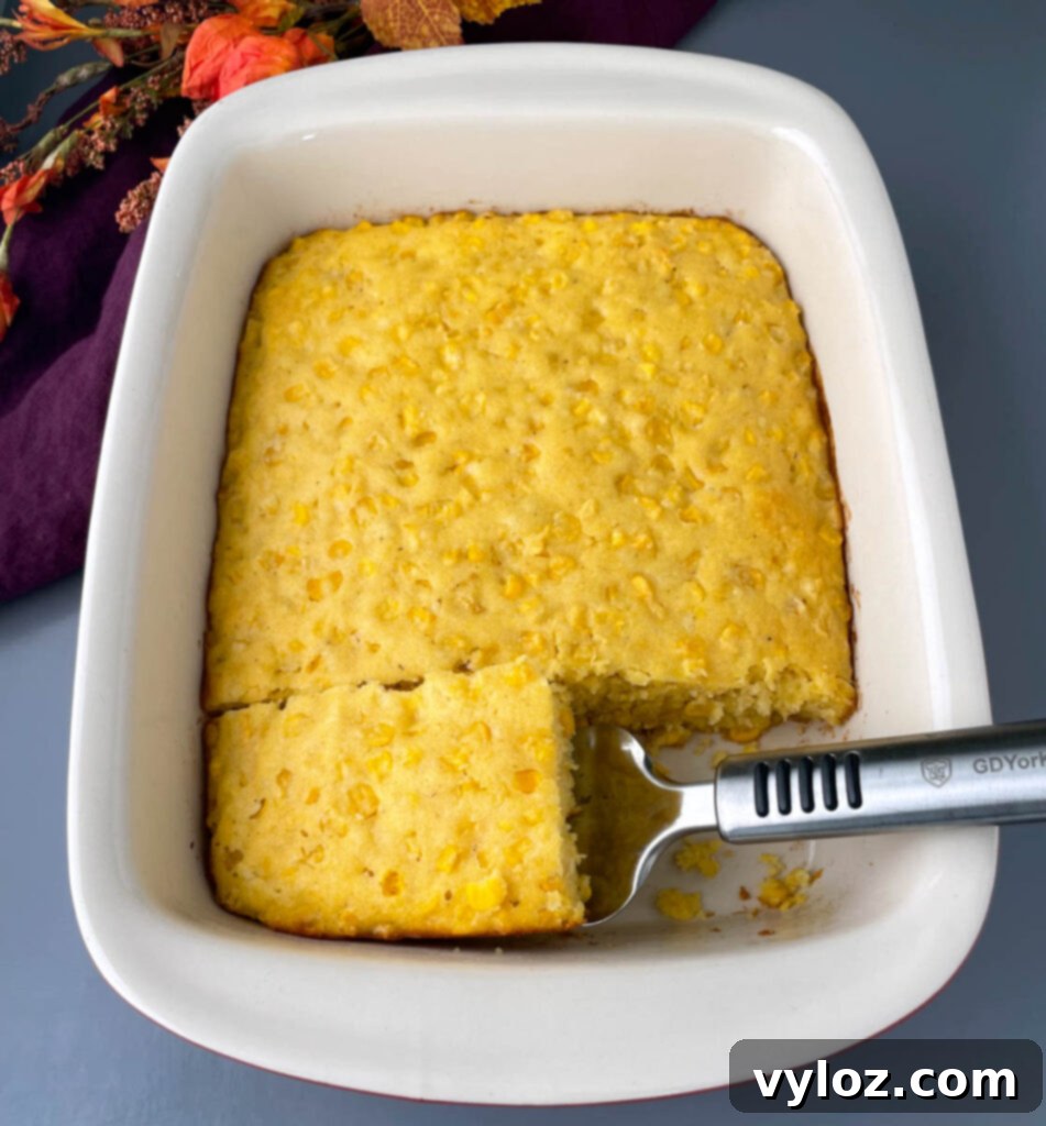 A perfectly portioned slice of golden corn casserole, showing its fluffy texture, still resting in the baking dish.