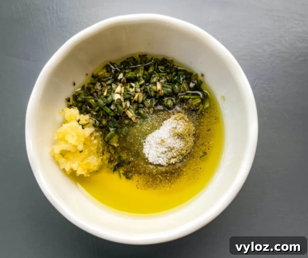 Close-up of a bowl filled with a fragrant mixture of minced garlic, olive oil, rosemary, and oregano, ready for seasoning.