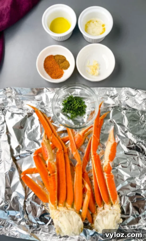 Easy Air Fryer Crab Legs 3 Ingredients for air fryer crab legs: butter, olive oil, Cajun seasoning, Old Bay Seasoning, minced garlic, and fresh snow crab legs on a flat surface.