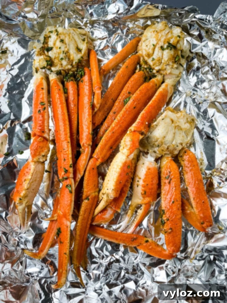 Easy Air Fryer Crab Legs 4 Fresh snow crab legs arranged on foil, generously brushed with garlic butter sauce before air frying.