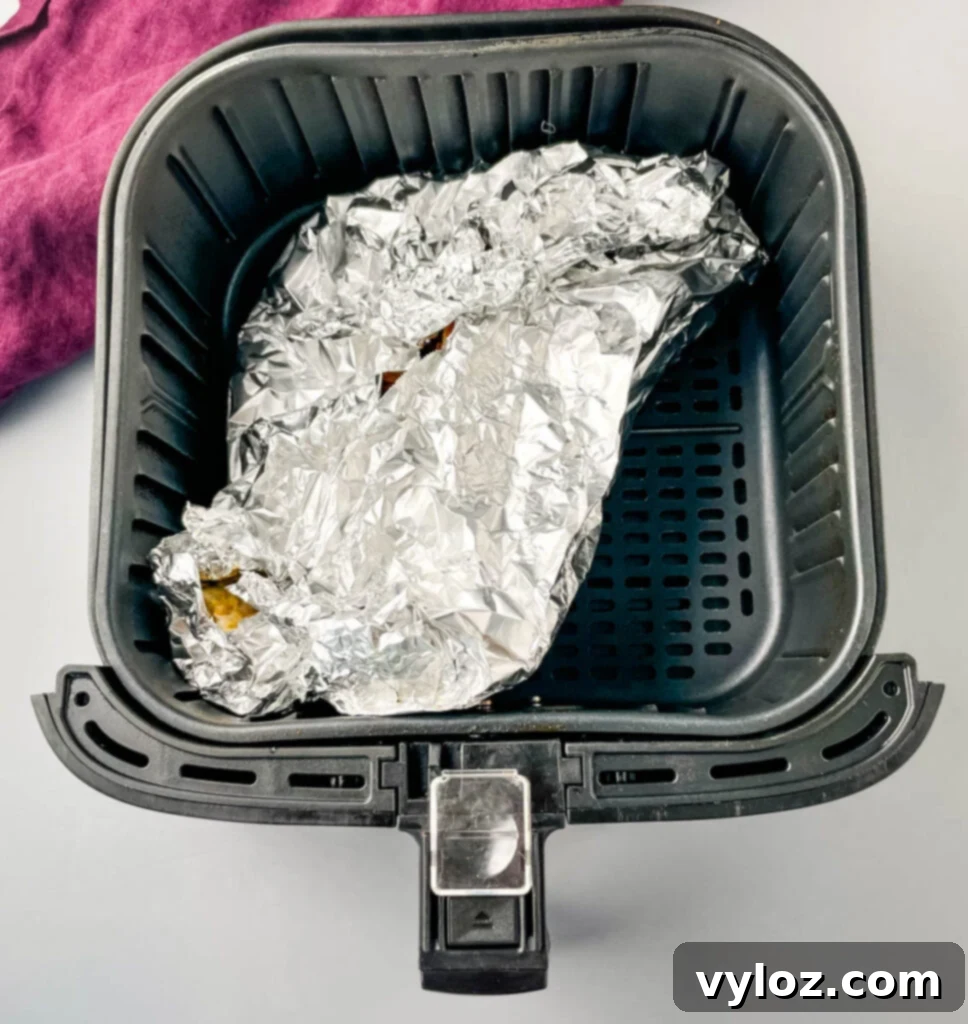 Easy Air Fryer Crab Legs 5 Crab legs carefully arranged in an air fryer basket, lined with foil, seasoned and ready for cooking.