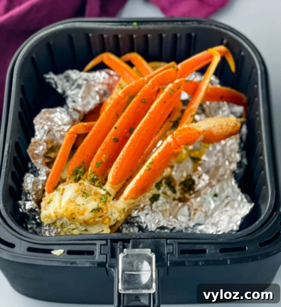 Easy Air Fryer Crab Legs 6 Foil-wrapped crab legs placed inside an air fryer basket, ready for cooking.