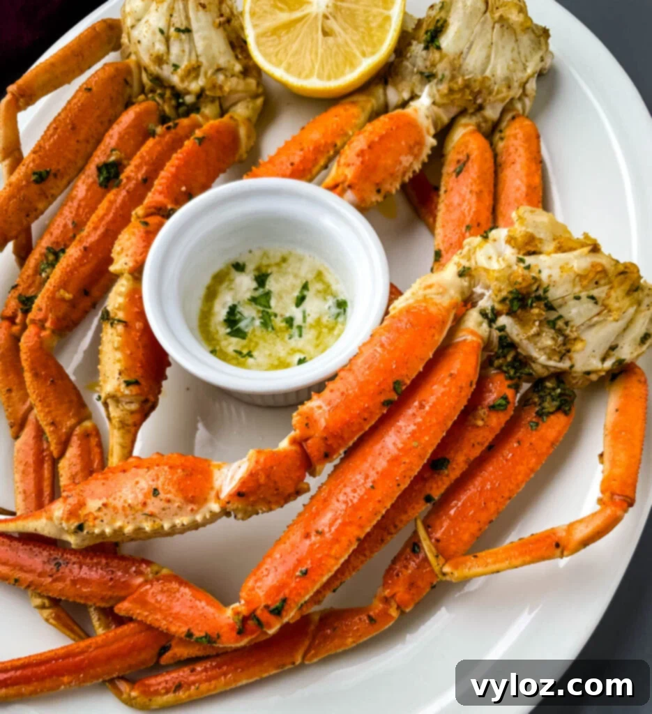 Easy Air Fryer Crab Legs 9 Air fryer crab legs on a white plate, served with a bowl of melted butter for dipping and lemon wedges.