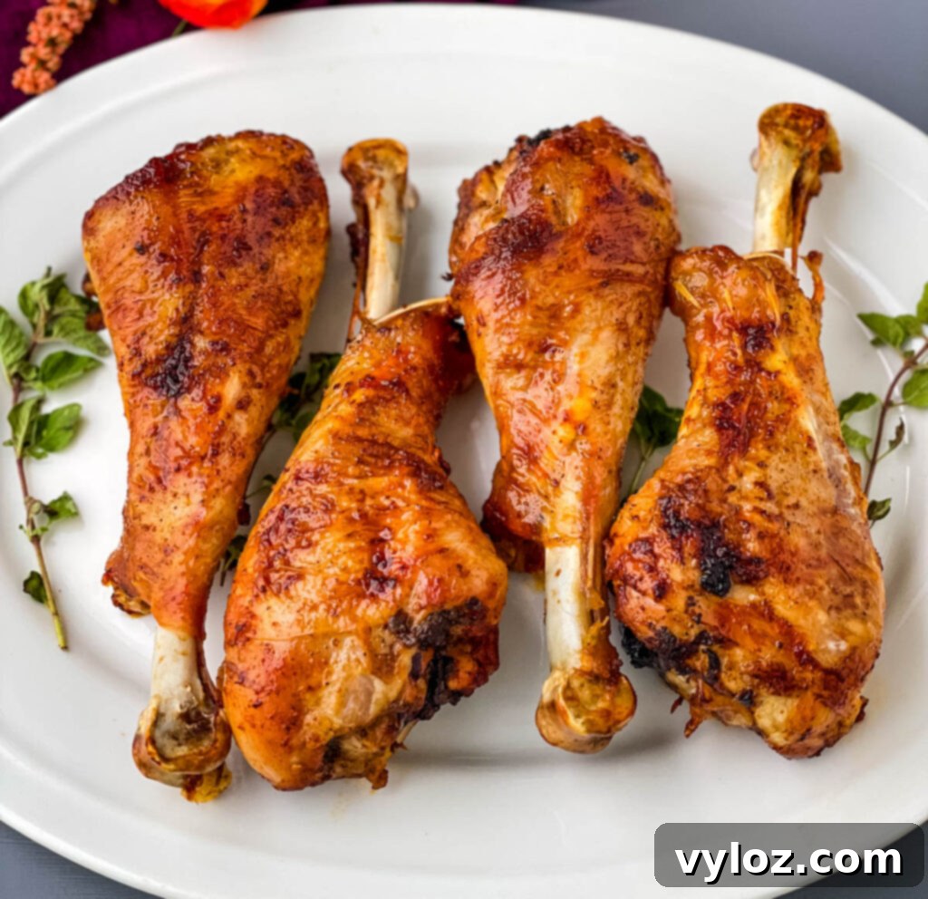 Perfectly cooked air fryer turkey legs resting on a white plate, showcasing their golden-brown, crispy skin.