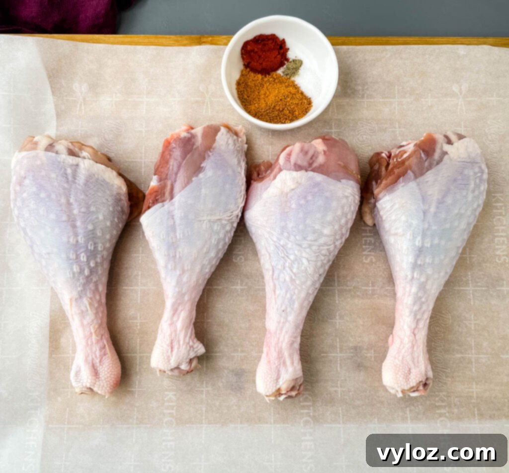 Raw turkey legs arranged on parchment paper, surrounded by a small bowl of mixed seasonings, ready for preparation.