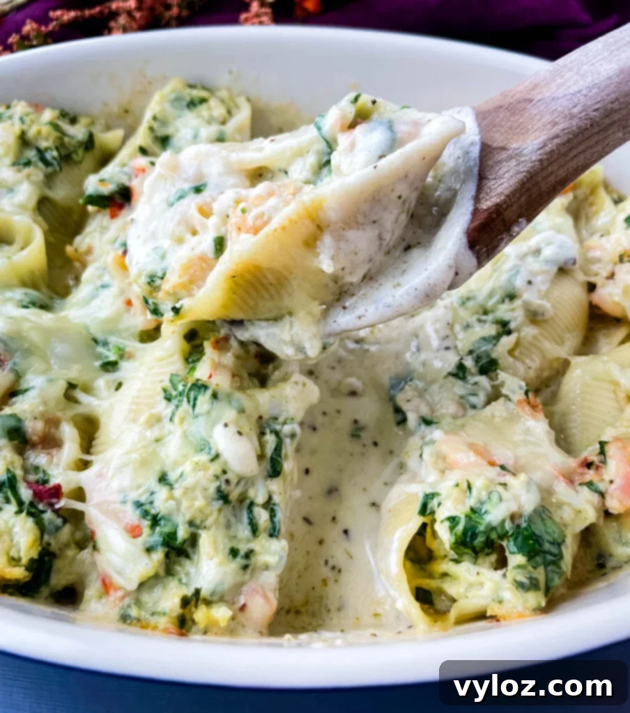 A wooden spoon holding seafood lobster, shrimp, and crab stuffed shells in a baking dish, showcasing the rich, creamy filling.