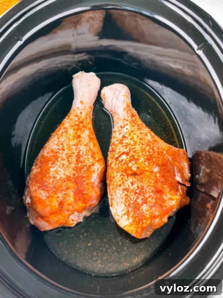 Two seasoned raw turkey legs placed inside a Crockpot slow cooker, ready for cooking