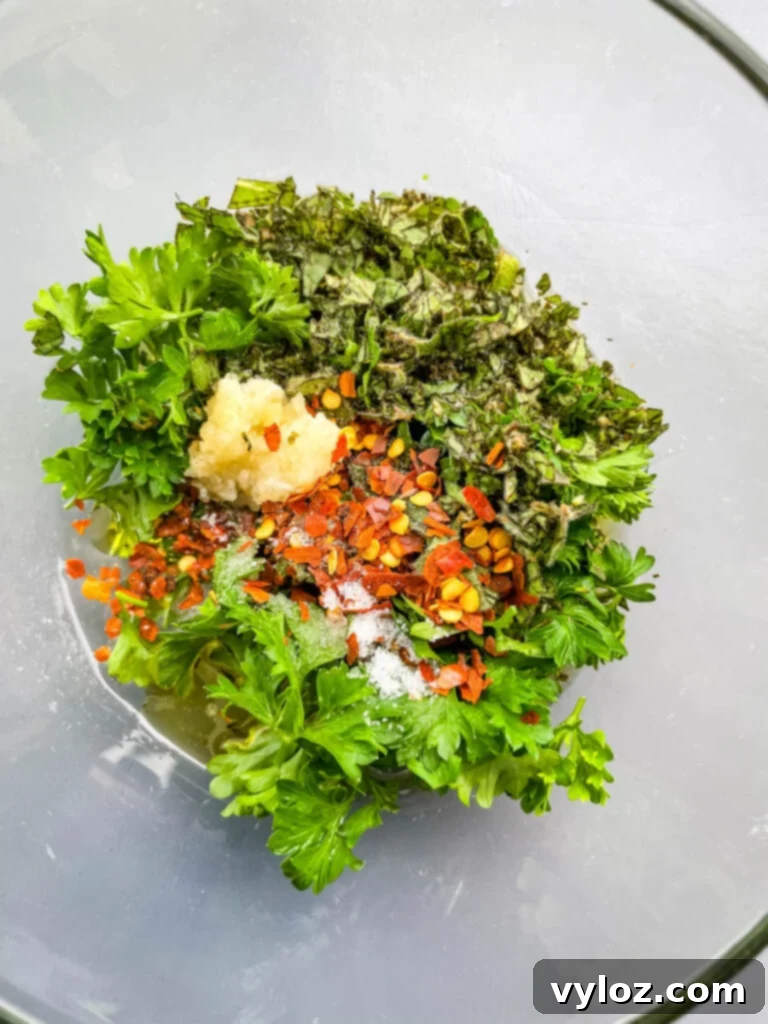 Fresh herbs and spices in a glass bowl, ready to be blended into chimichurri sauce.