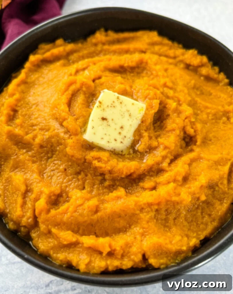 Mashed sweet potatoes in a rustic bowl, garnished with a pat of butter and brown sugar, set against a warm background