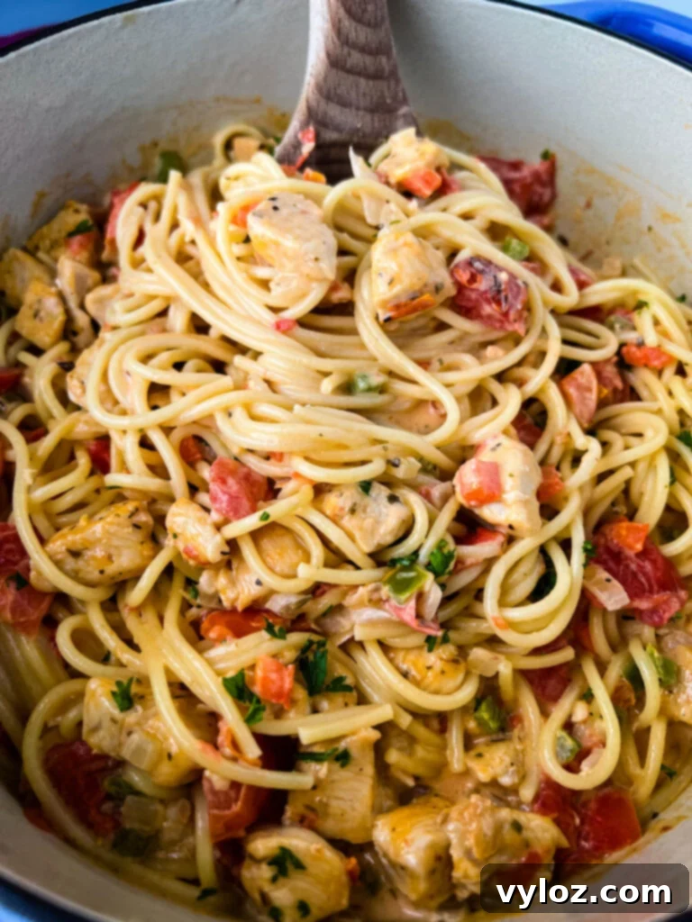 southern chicken spaghetti in a Dutch oven with a wooden spoon, garnished with fresh herbs
