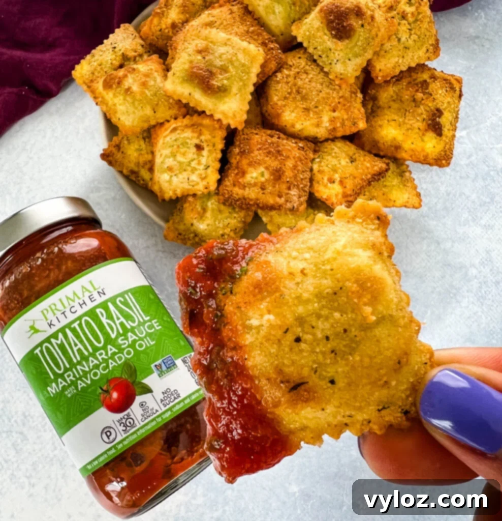 A hand holding a plate with air fryer toasted fried ravioli and a small bowl of marinara sauce