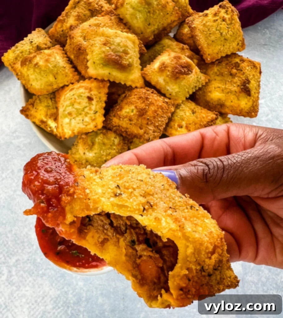 Person holding a plate with toasted fried ravioli and a small bowl of marinara sauce, showcasing the meal