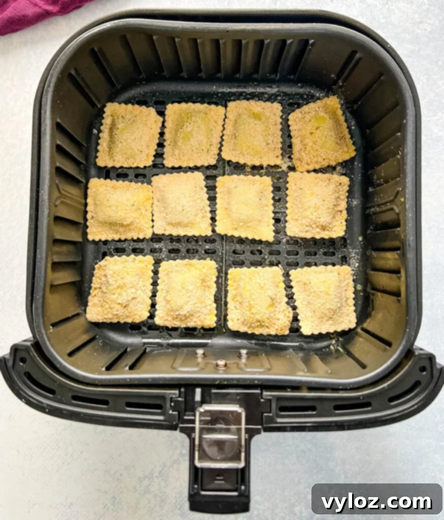 Breaded ravioli cooking inside an air fryer basket, turning golden brown
